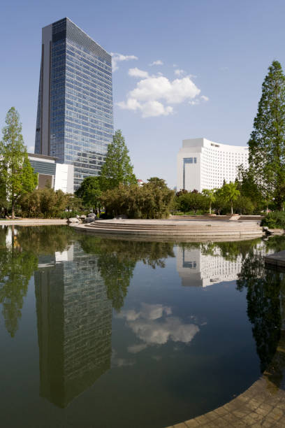 Lake in a park in Beijing, China, with tall modern buildings in the background and reflected in the water of the lake. There is quite a lot of dust floating on the surface of the water.