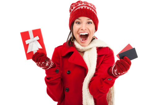 Photo of an attractive young woman in red coat, mittens and knit hat, holding two gift cards and gift box with a huge smile on her face. Selective focus on blank gift/credit cards and box.