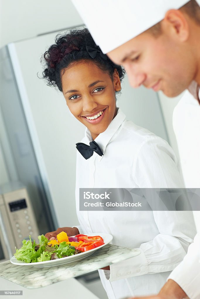 Male chef preparing food while a waitress holding fresh salad  20-24 Years Stock Photo