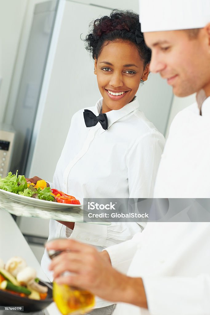 Mâle chef préparer à manger tandis que la serveuse tenir salade fraîche - Photo de 20-24 ans libre de droits