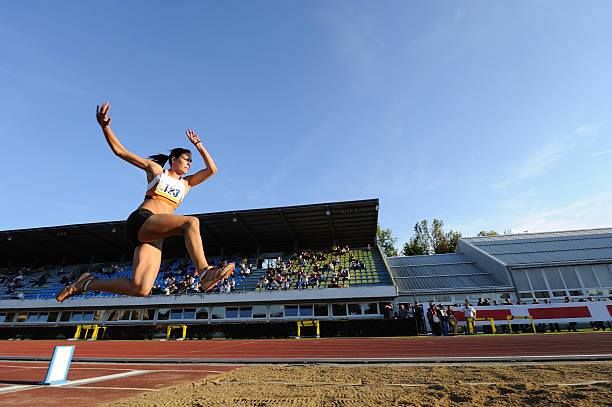 Female athlete jumping Side view of young female athlete in mid-air at long jump long jump stock pictures, royalty-free photos & images