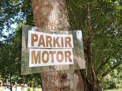 sign of parking area for motorbike in Indonesian language. the sign attached on tree trunk