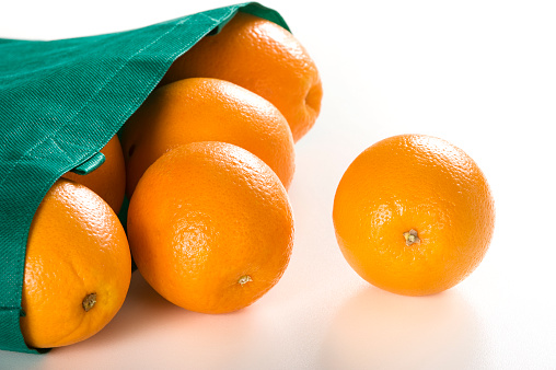 Several oranges roll out of an environmentally friendly green bag.  Click to view similar images.