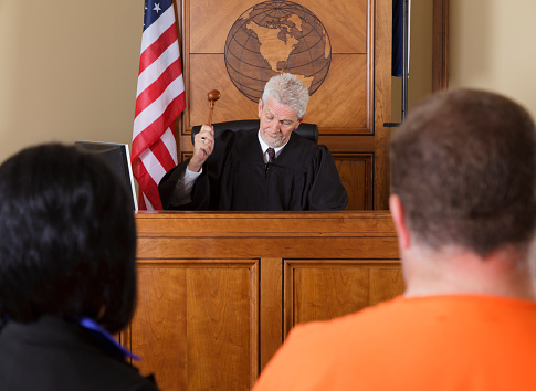 A judge as seen from behind the criminal defendant and his lawyer in a courtroom.