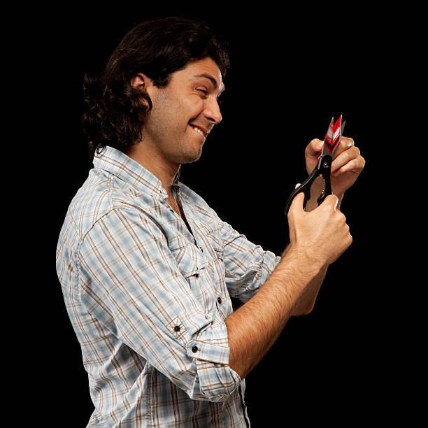 Man Grimaces While Cutting Up His Credit Card with Scissors stock photo