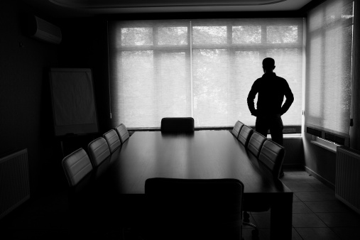 Silhouette Of Lonely Businessman Standing By Boardroom Table In Office.The chairs around table are empty.He looks desperate.The black and white color and dark atmosphere is used for economic depression feel.Full frame DSLR camera was used in real office. 