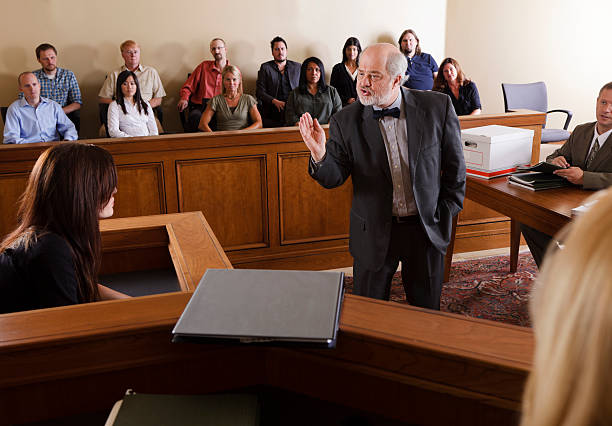 Asian lawyer in a formal suit works alone at his desk with a wooden gavel, laptop, paperwork, tablet, and calculator, focusing on home and land mortgage regulations.