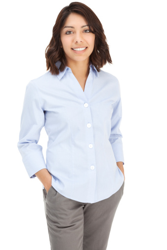 Photo of an attractive young Hispanic businesswoman in blue button-down shirt, standing with hands in pockets; isolated on white.