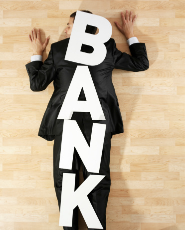 Large letters forming “bank” message on top of a businessman laying on floor