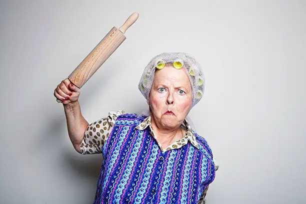 senior woman with curler and old ashioned coat,raising rolling pin, vey angry, mihgt be going to beat someone