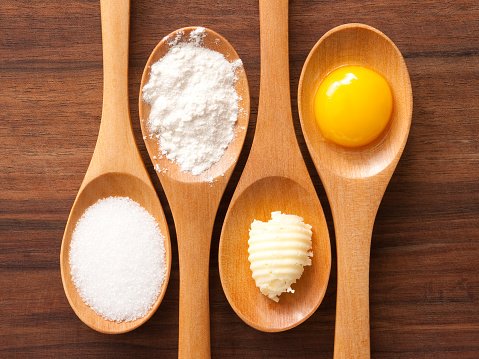 Top view of wooden spoons containing baking ingredients (sugar, flour, butter, egg)
