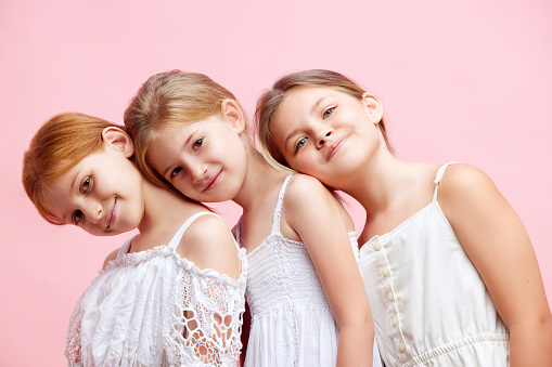 Portrait of beautiful little girls, children posing together against pink studio background. Well-being, care free time. Concept of skincare, childhood, cosmetology and health, beauty, ad