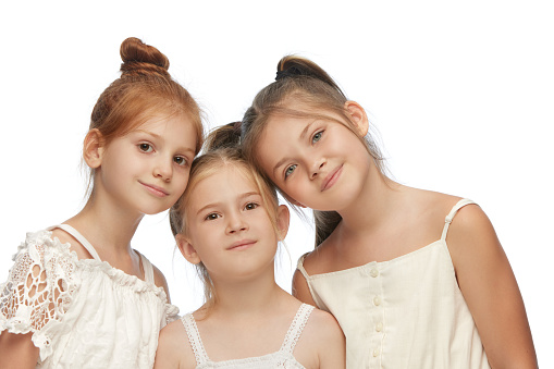 Portrait of beautiful, attractive little girls, children posing together, looking at camera against white background. Concept of childhood, fashion, family, emotions, lifestyle, care, happiness, ad