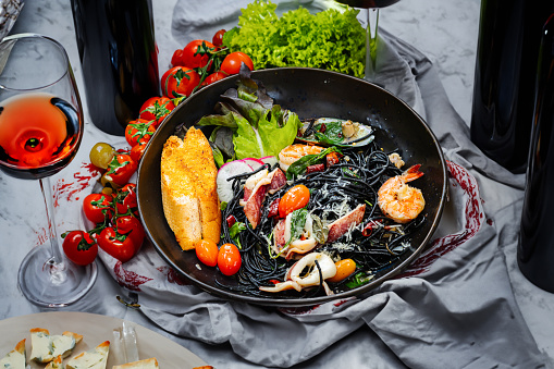 Charcoal spaghetti stir-fried with seafood placed on the dining table with a glass of wine and fresh vegetables.