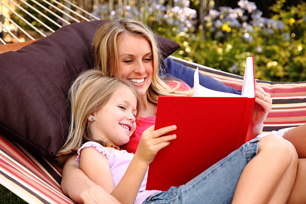 A mother and her daughter reading a big book in a hammock XXXL. Mother and daughter relaxing outdoors in a hammock reading a book. gchutka stock pictures, royalty-free photos & images