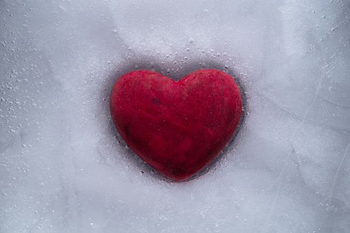Red stone heart with a cracks frozen in ice. Symbol of love or betrayal or separation.