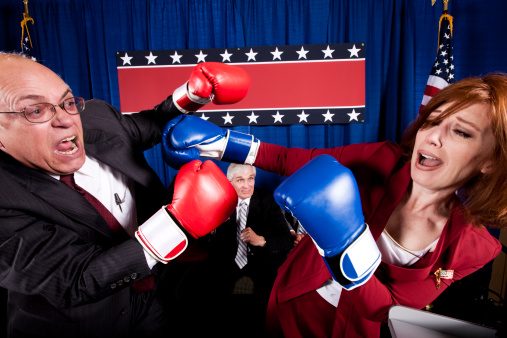 Two mature politicians (one male, one female) engage in a heated debate which turns into a conflict and then escalates into a full-blown boxing match.