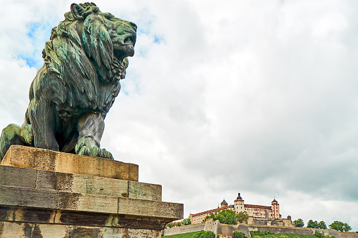 Wuerzburg, Germany - July, 28, 2023: Lion figure on the Luitpold Bridge in the background the Marienberg Fortress.
