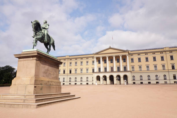 People sit and walk in front of The Royal Palace in downtown Oslo, Norway on a sunny morning.