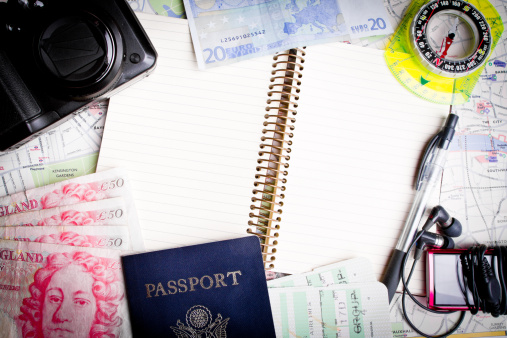 White center background for copy space with various travel items around the perimiter including passport, notebook, pen, euros, british pounds and compass