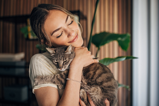 Young woman holding a cat at home.