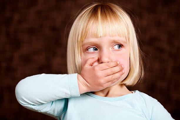 beautiful blonde toddler makes 'speak no evil' sign - hand voor de mond stockfoto's en -beelden