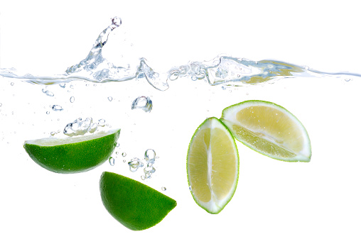 Fresh lime quarters falling into the cold water and splashing, isolated on white background. Splashing and bubbles visible.