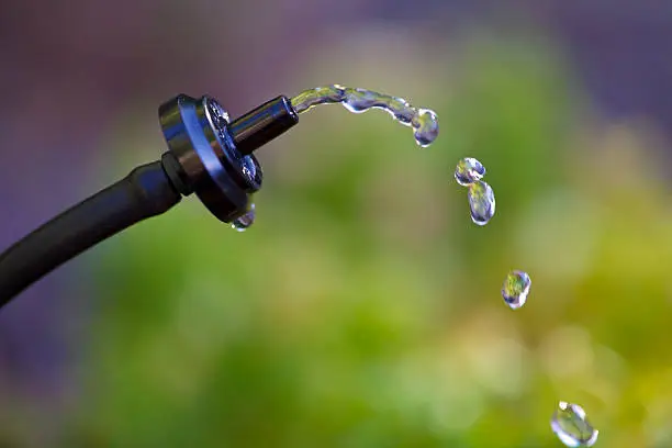 A closeup of a watering system dripper (emitter) with drops of water suspended in the air. Very shallow focus on emitter.