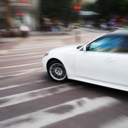 Car on zebra crossing. Motion blur from panning. Focus on front wheel. Lotogype and other features removed or modified.