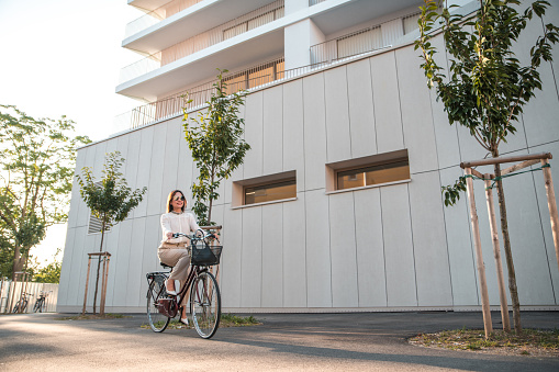 Caucasian businesswoman  riding a bicycle to work. She is wearing smart casual clothing arriving to the office in a business district.