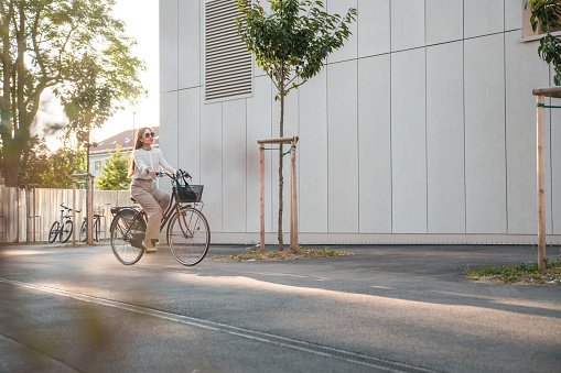 Caucasian businesswoman  riding a bicycle to work. She is wearing smart casual clothing arriving to the office in a business district.