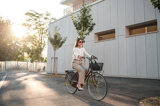 Caucasian businesswoman  commuting to work by riding a bicycle. She is wearing smart casual clothing arriving to the office in a business district.
