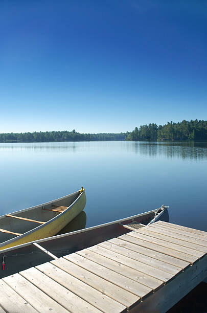 Two canoes docked on a still lake in the Kawartha region of Ontario, Canada. This early morning scene is familiar to thousands of Canadians vacationing in 'Cottage country'. A fishing rod awaits in the closest canoe.
