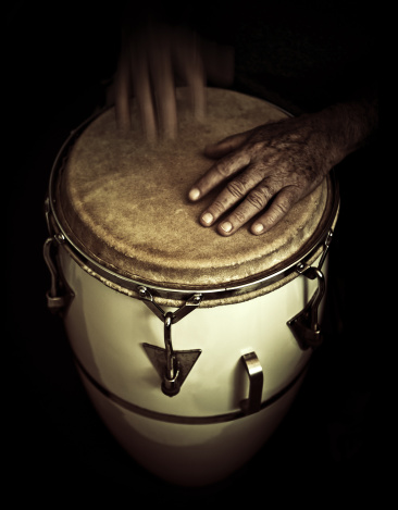 old man hands playing latin percussion (tumbadora or congas) one hand in focus, left one moving and defocussed