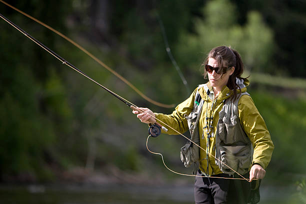 Woman in nature fly fishing for trout wearing sunglasses stock photo