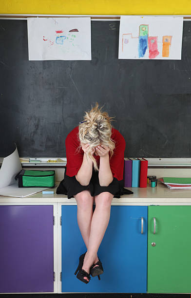 Exhausted teacher sitting on counter in brighly colored classroom stock photo