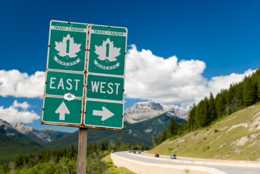 Roadsign for the Trans-Canada highway with the highway in the background. A few cars drive the highway with a beautiful view of the canadian rockies.