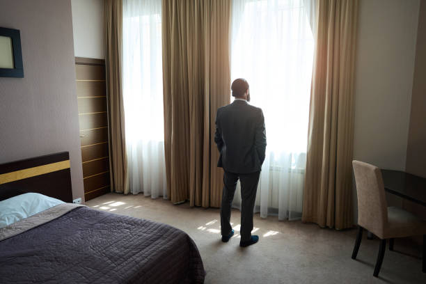 istock Hotel guest stands at the window in the sleeping area 1576460275