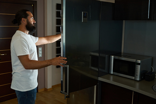 Man in jeans takes something out of a large refrigerator, next to a microwave