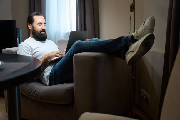 istock Middle-aged male is located on the sofa with a laptop 1576461802