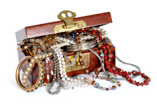 Close-up photo looking down at a wooden treasure chest over-flowing with jewels, pearls, beads and white chicken eggs isolated on a white background. Copy space