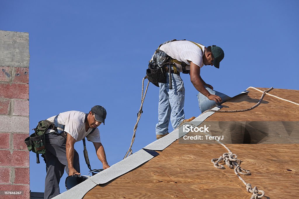 Dangerous Jobs Roofers on an 8-12 pitch roof laying under-layment before installing roof tile.  Roofer Stock Photo