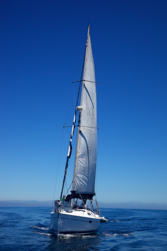 Fiberglass newer model sailboat comes up on a stern at sea of Southern California waters in the Santa Monica Bay, three unrecognizable people