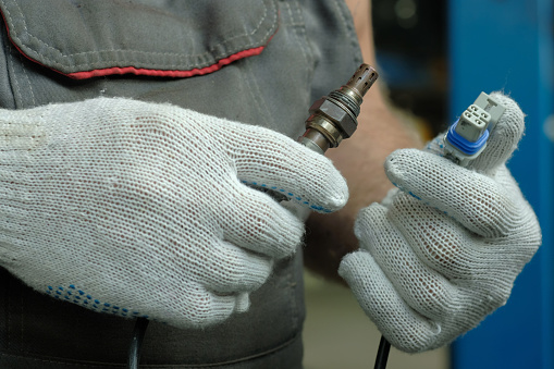 An auto mechanic holds a new oxygen sensor in his hands.