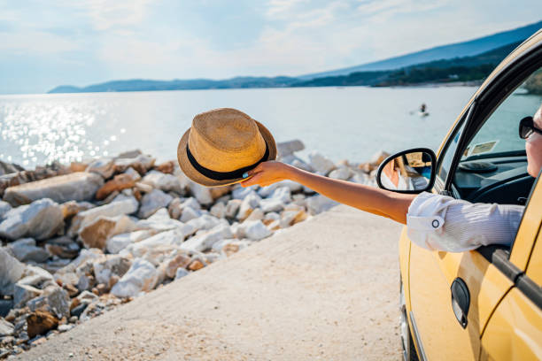 istock Woman holding a hat outside the open car window on vacation 1576466514