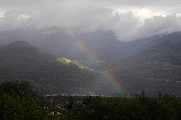 A rainbow reaching a small village in the mountains with clouds above the mountains