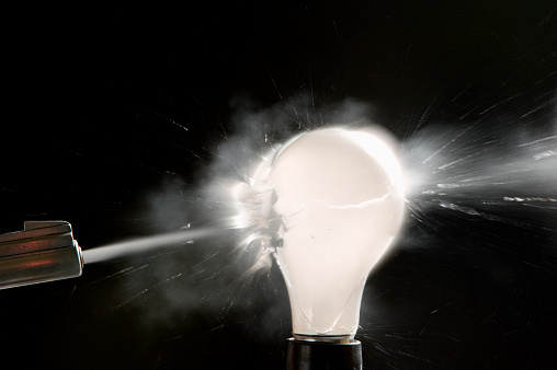 A bullet passes through a light bulb causing it to explode.  Lots of debris flying and gas from the bulb.  This is all in camera, no special effects.  Click to view similar images.