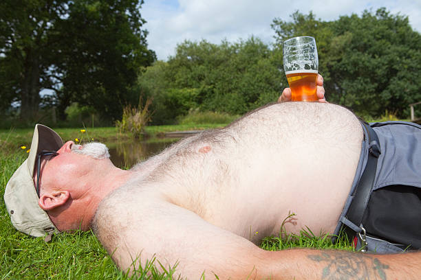 obese mann mit einem glas bier zum sonnenbaden - pot belly stock-fotos und bilder