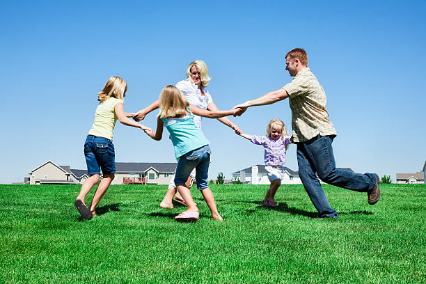 Ring Around The Rosy Photo of a young family of five enjoying a warm summer day in a grassy neighborhood park, playing Ring Around The Rosie. mormon woman photos stock pictures, royalty-free photos & images