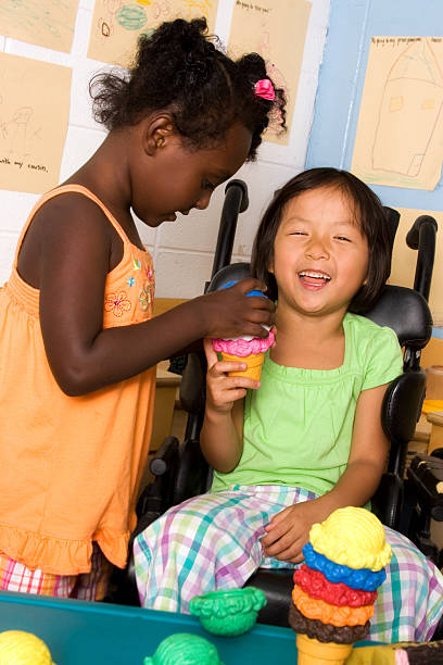 Classmate helping friend Little girl playing with friend in wheelchair at preschool social inclusion photos stock pictures, royalty-free photos & images